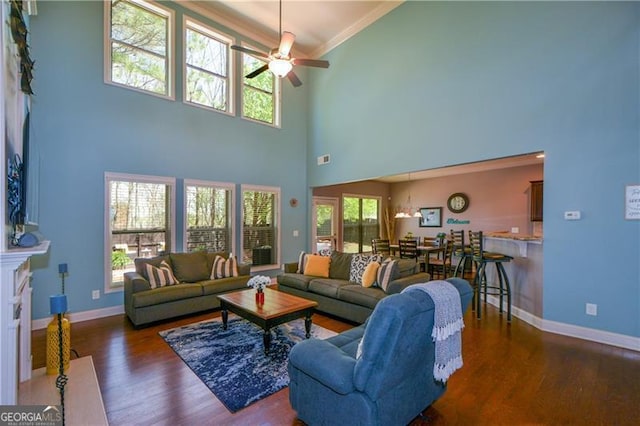 living area featuring a towering ceiling, baseboards, crown molding, ceiling fan, and wood finished floors