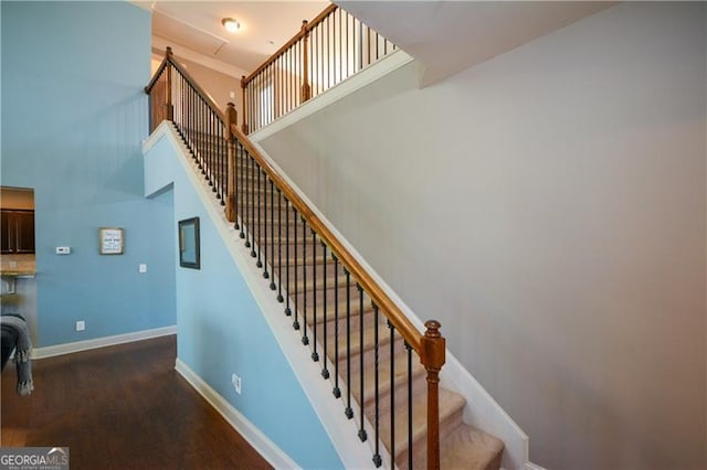 staircase with baseboards, a high ceiling, and wood finished floors