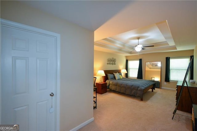 bedroom with a raised ceiling, ceiling fan, light colored carpet, and baseboards