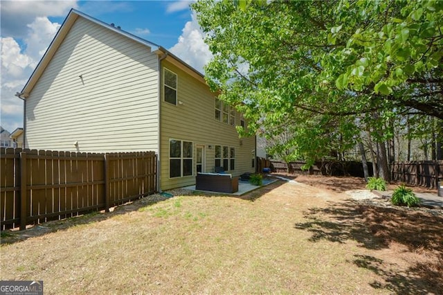 back of property featuring a yard, a fenced backyard, and a hot tub