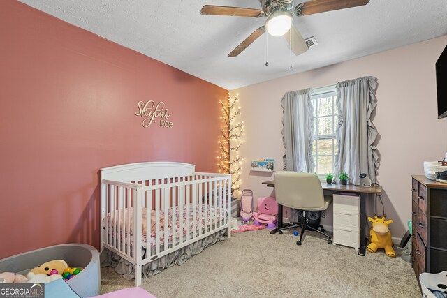 bedroom featuring a nursery area, a ceiling fan, visible vents, and carpet