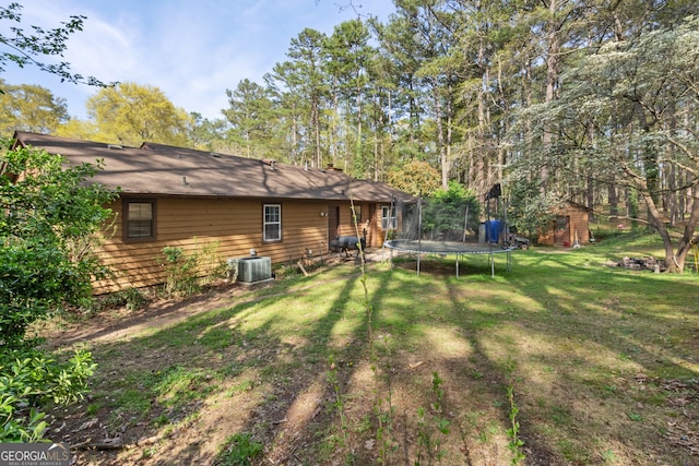 view of yard featuring an outdoor structure, a trampoline, a shed, and central AC unit