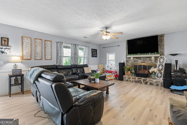 living room featuring a fireplace, light wood-style floors, a textured ceiling, and ceiling fan