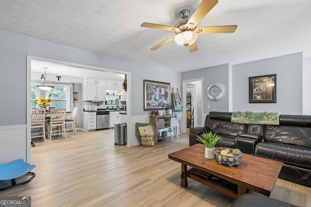living room featuring a ceiling fan, a wainscoted wall, a textured ceiling, and light wood-style flooring