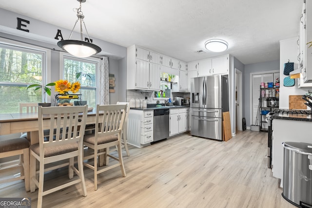 kitchen with white cabinets, stainless steel appliances, dark countertops, light wood-style floors, and decorative backsplash