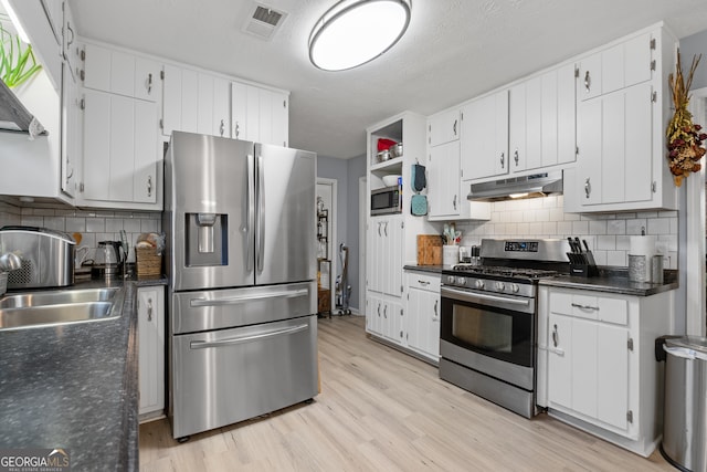 kitchen featuring dark countertops, a sink, appliances with stainless steel finishes, light wood-style flooring, and under cabinet range hood