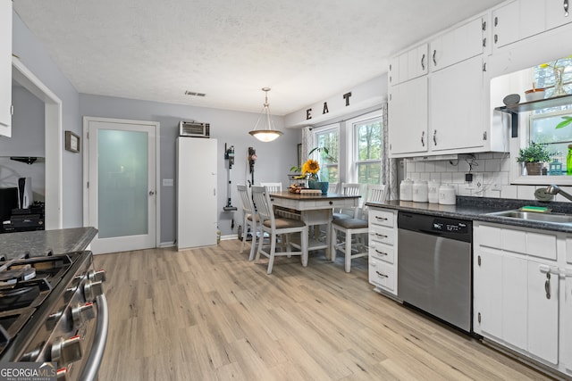 kitchen featuring dark countertops, a sink, light wood-type flooring, appliances with stainless steel finishes, and white cabinetry