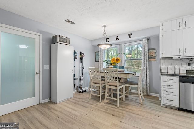 dining room featuring baseboards, light wood finished floors, a textured ceiling, and visible vents