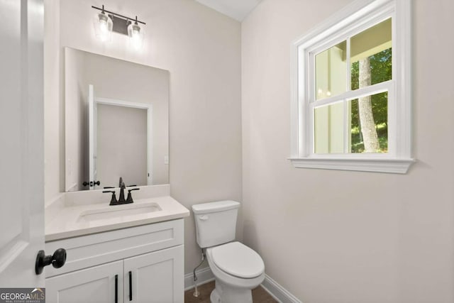 half bathroom with baseboards, toilet, and vanity