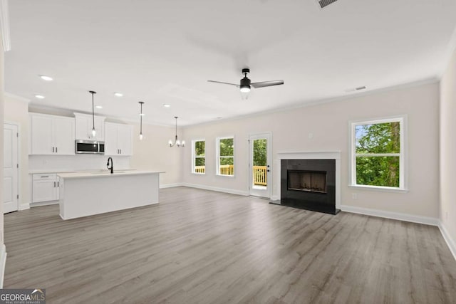 unfurnished living room featuring baseboards, a fireplace with raised hearth, light wood-style flooring, and ceiling fan with notable chandelier
