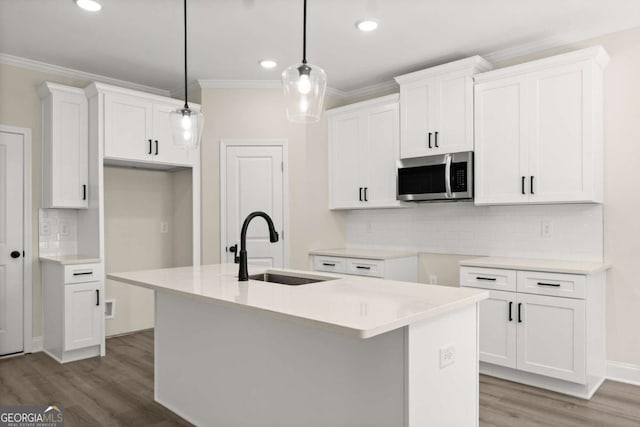 kitchen with stainless steel microwave, a center island with sink, a sink, and ornamental molding