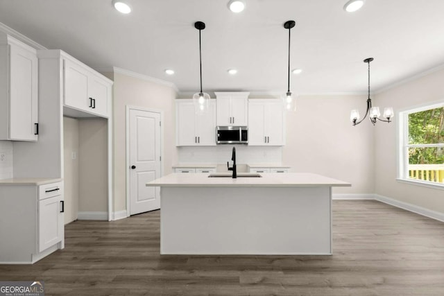 kitchen with tasteful backsplash, stainless steel microwave, ornamental molding, a sink, and a kitchen island with sink