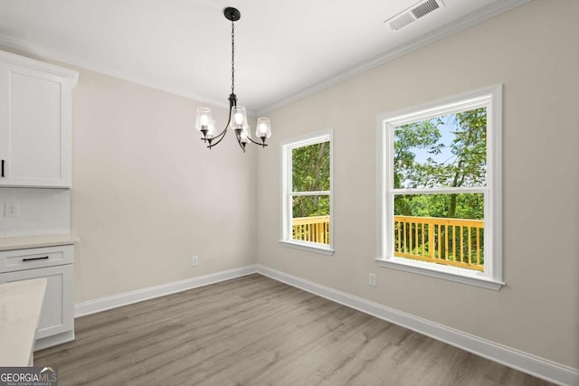 unfurnished dining area with a notable chandelier, crown molding, light wood-style flooring, baseboards, and visible vents