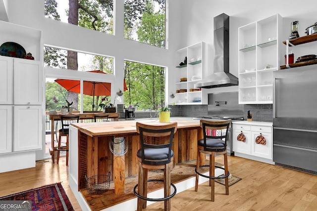 kitchen with wall chimney range hood, open shelves, high quality fridge, and a towering ceiling