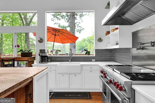 kitchen with a sink, light countertops, extractor fan, white cabinetry, and double oven range