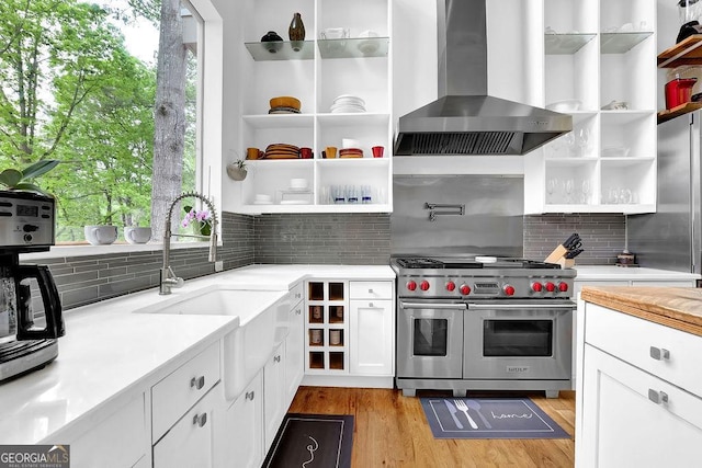 kitchen featuring wall chimney range hood, double oven range, open shelves, a sink, and white cabinets