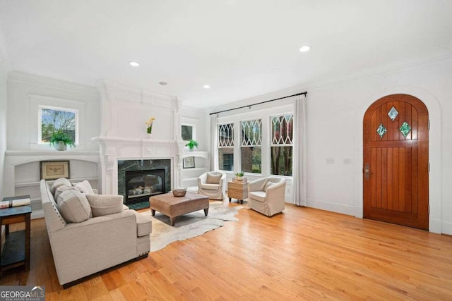 living room featuring plenty of natural light, crown molding, light wood-style floors, and a premium fireplace