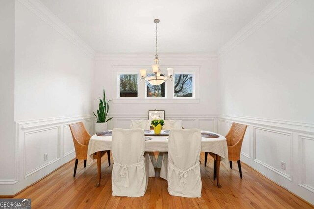 dining room with a decorative wall, ornamental molding, a chandelier, and light wood-type flooring