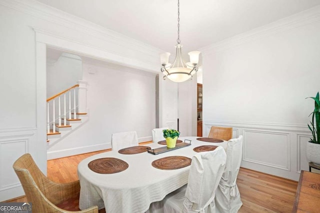 dining space with crown molding, stairs, an inviting chandelier, a decorative wall, and light wood-style flooring