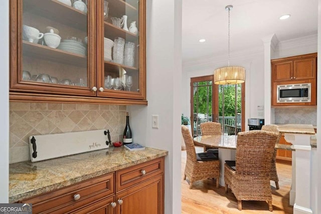 kitchen featuring stainless steel microwave, ornamental molding, light wood-style flooring, light stone countertops, and brown cabinetry