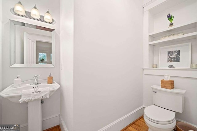 half bathroom with toilet, baseboards, and wood finished floors