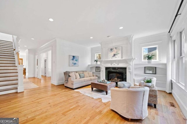 living room with stairway, a fireplace, light wood-style floors, ornamental molding, and recessed lighting