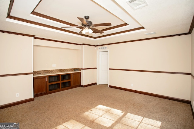 spare room featuring a tray ceiling, visible vents, a ceiling fan, crown molding, and light colored carpet