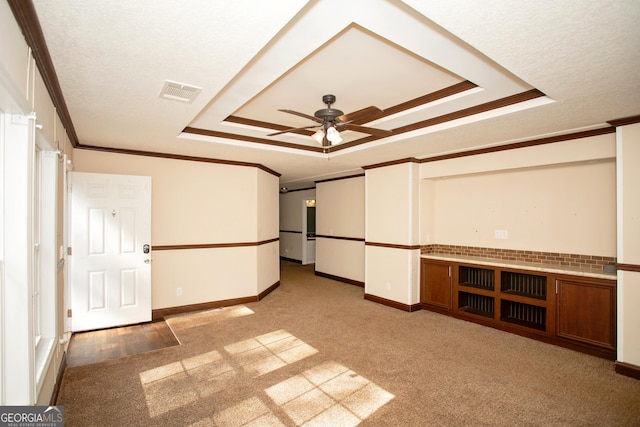 interior space featuring a raised ceiling, carpet floors, visible vents, and ornamental molding