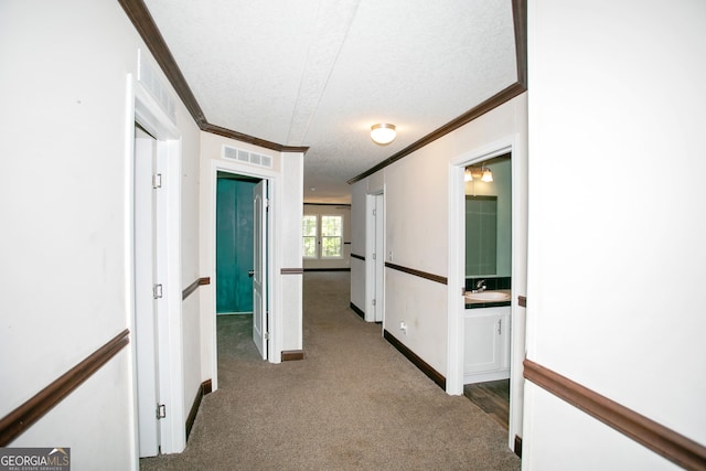hallway featuring a sink, baseboards, visible vents, carpet floors, and ornamental molding