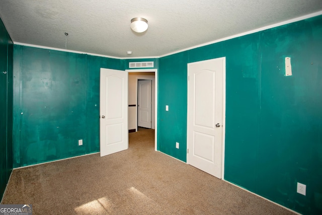 unfurnished bedroom with crown molding, a textured ceiling, visible vents, and carpet
