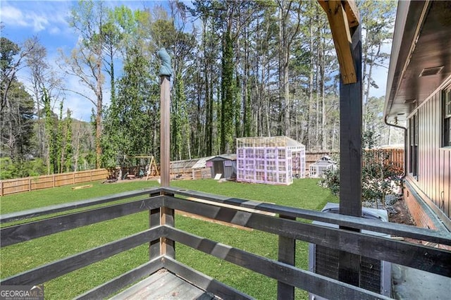 wooden terrace with a storage shed, an outbuilding, a fenced backyard, and a lawn