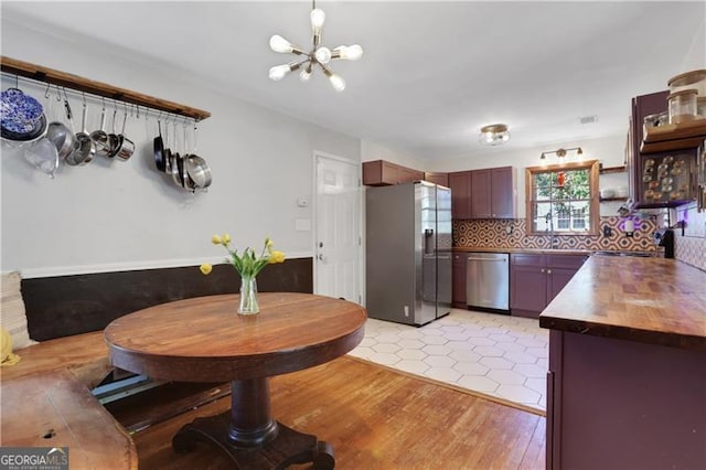kitchen with an inviting chandelier, a sink, light wood finished floors, stainless steel appliances, and decorative backsplash