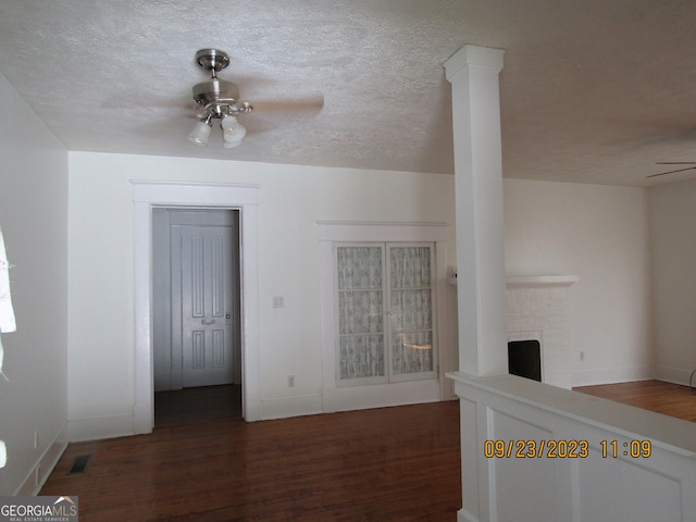unfurnished living room with a ceiling fan, wood finished floors, a brick fireplace, a textured ceiling, and visible vents