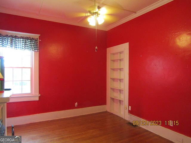 spare room with baseboards, ornamental molding, built in shelves, wood finished floors, and a ceiling fan