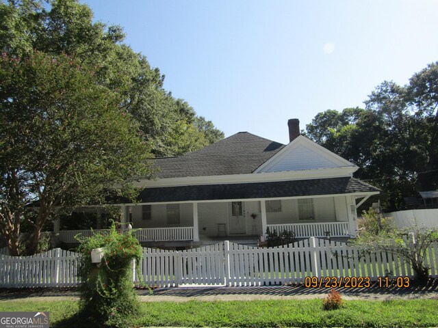 rear view of house with a chimney, a fenced front yard, a porch, and roof with shingles