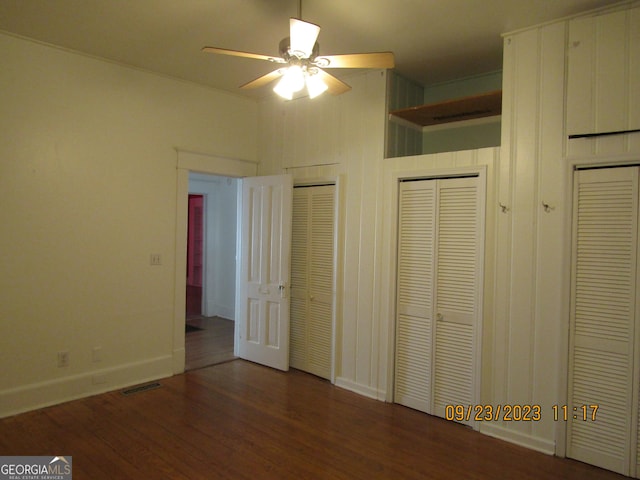 unfurnished bedroom featuring two closets, baseboards, visible vents, ceiling fan, and wood finished floors