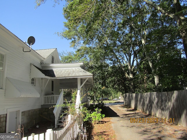 view of property exterior featuring covered porch, driveway, a shingled roof, and fence