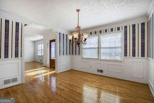 unfurnished dining area with a decorative wall, visible vents, a chandelier, and a textured ceiling