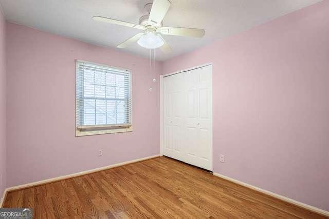 unfurnished bedroom featuring baseboards, a closet, wood finished floors, and ceiling fan