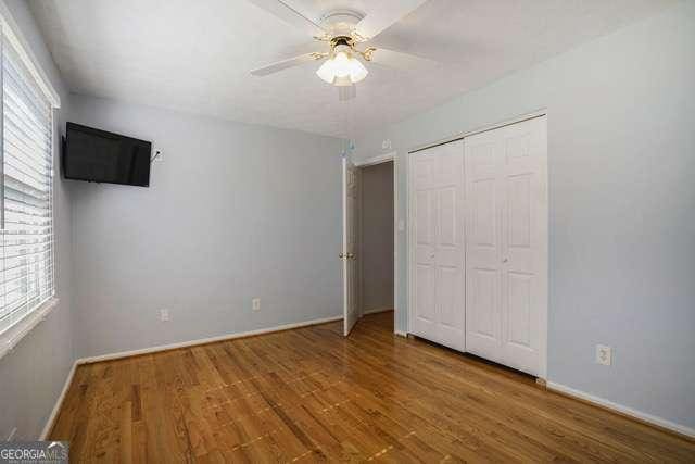 unfurnished bedroom with baseboards, a closet, wood finished floors, and ceiling fan