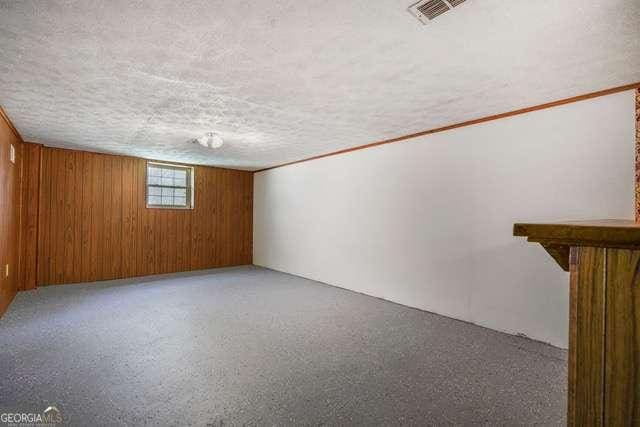 below grade area with light carpet, a textured ceiling, wooden walls, and visible vents