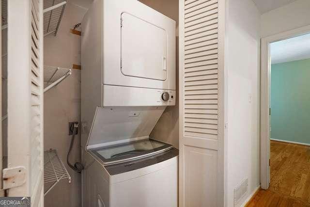 clothes washing area with wood finished floors, stacked washer / dryer, and laundry area