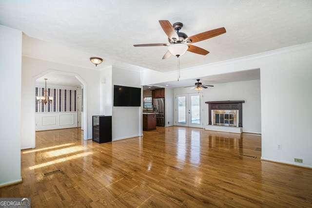 unfurnished living room with arched walkways, wood finished floors, ceiling fan, and ornamental molding