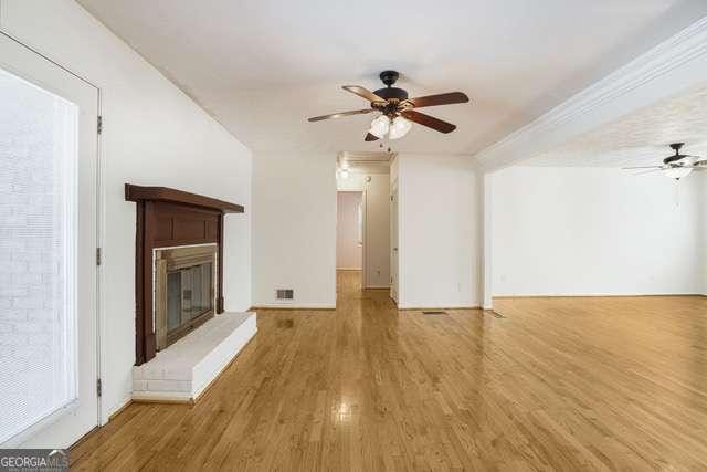 unfurnished living room featuring a ceiling fan, wood finished floors, a glass covered fireplace, and visible vents