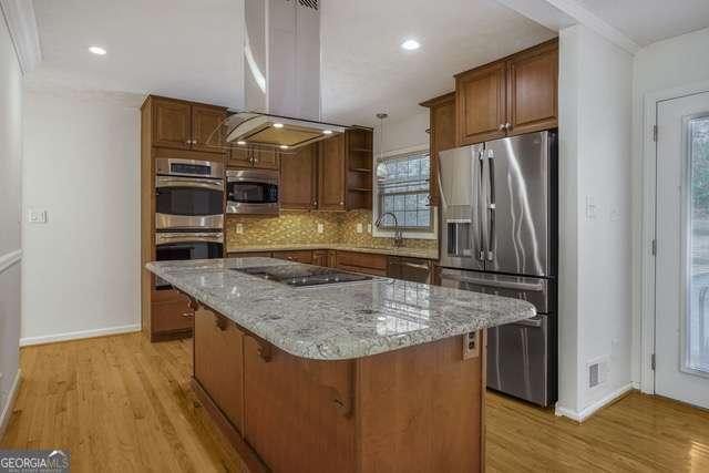 kitchen featuring light wood-style flooring, island exhaust hood, appliances with stainless steel finishes, a sink, and backsplash