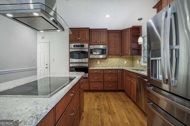 kitchen with wall chimney exhaust hood, stainless steel appliances, a sink, light wood-type flooring, and backsplash