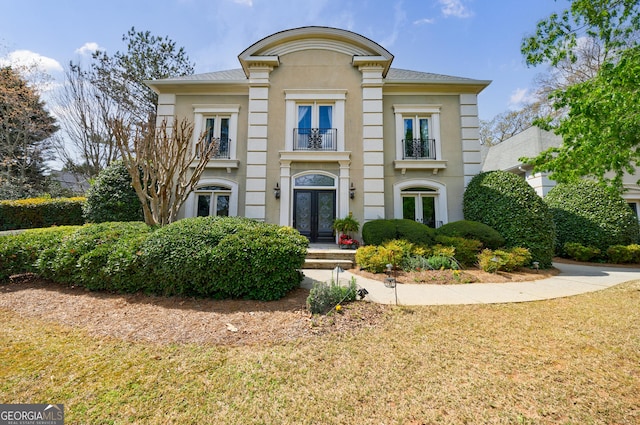 view of front of home featuring french doors, stucco siding, a front lawn, and a balcony