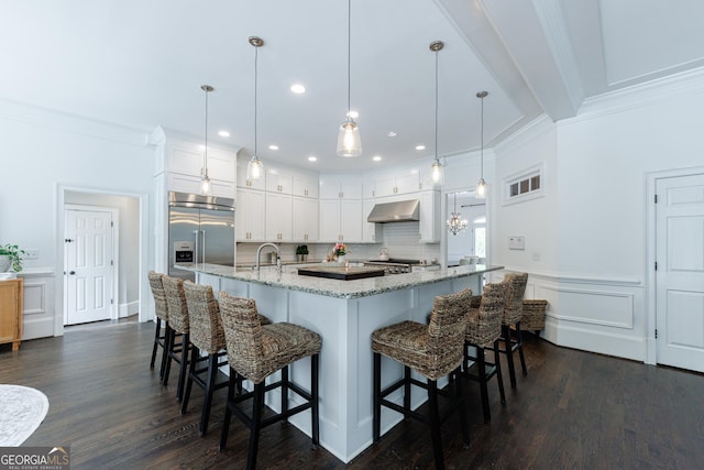 kitchen featuring crown molding, built in refrigerator, a kitchen breakfast bar, and white cabinets