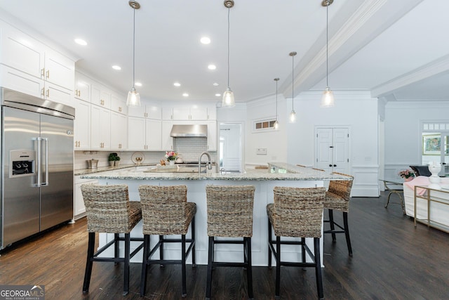 kitchen with dark wood-style flooring, built in refrigerator, white cabinets, ornamental molding, and under cabinet range hood