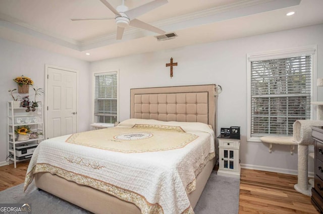 bedroom with a tray ceiling, wood finished floors, visible vents, ornamental molding, and recessed lighting